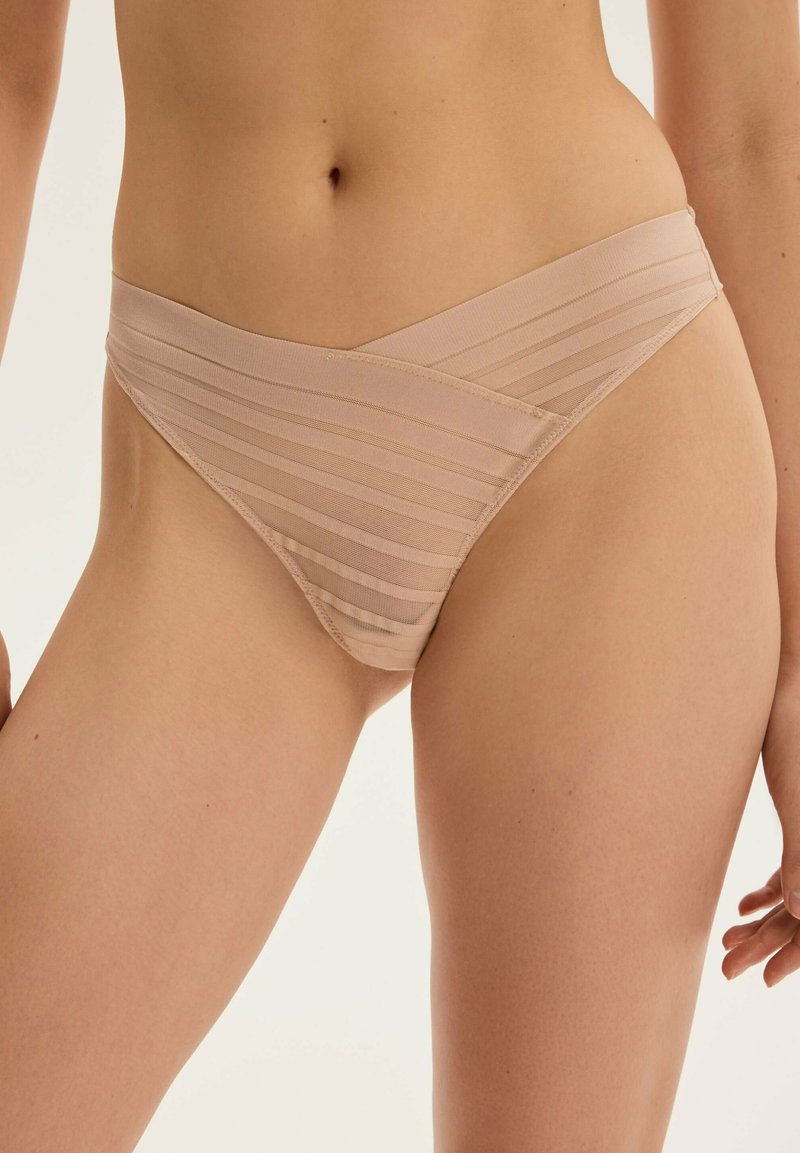 Majtki w kolorze nude, wykonane z gładkiego, elastycznego materiału, z ukośnym paskiem na pasku. Charakteryzują się minimalnym zakryciem.