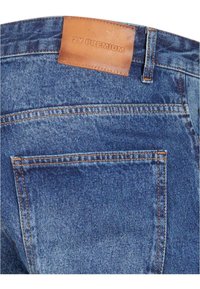 Jeans din denim albastru cu un patch din piele la brâu etichetat "2Y PREMIUM", cusături vizibile și un design clasic pentru buzunare.