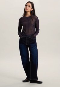 Top noir transparent à manches longues avec un motif texturé, associé à un jean droit taille haute bleu foncé avec des surpiqûres contrastantes. Ballerines noires.