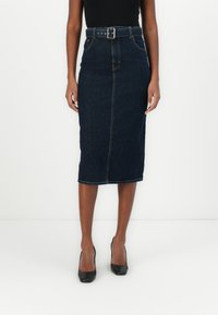 Jupe crayon en denim foncé, présente une silhouette ajustée, une taille haute ceinturée et un ourlet droit avec des bords légèrement effilochés.