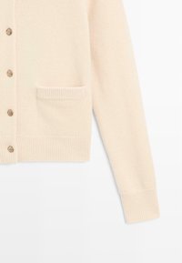 Cardigan beige chiaro in morbido tessuto, con scollatura a V, bottoni frontali, polsini a coste e una tasca sul lato sinistro.