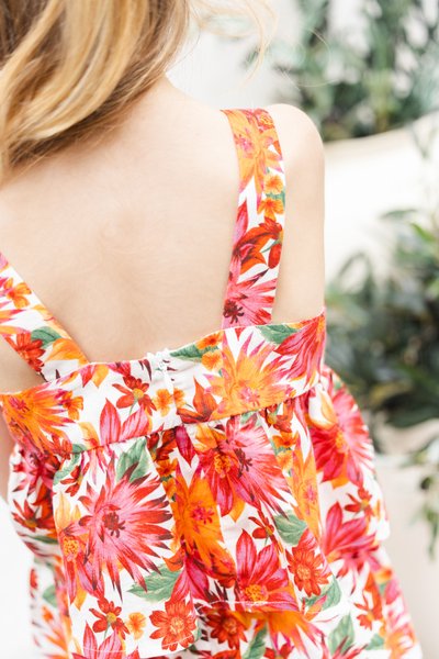 Φλοράλ φόρεμα με φωτεινά πορτοκαλί και κόκκινα λουλούδια σε λευκό φόντο. Διαθέτει φαρδιές τιράντες, στρωματοποιημένο σχέδιο και κλείσιμο με κουμπί στο πίσω μέρος.