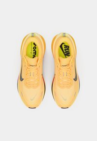 Φωτεινά κίτρινα αθλητικά παπούτσια με μαύρες λεπτομέρειες, διαθέτοντας επάνω μέρος από δίχτυ, υφή και μαλακή σόλα. Οι κορδόνια είναι κίτρινα· το λογότυπο είναι ορατό.