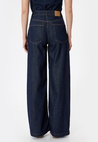 Laivaleikkaukset denim-mekot, tumma sininen, korkea vyötärö, näkyvät ompeleet ja kaksi takataskua. Vaaleanruskea nahkalaatta vyötärön kohdalla.