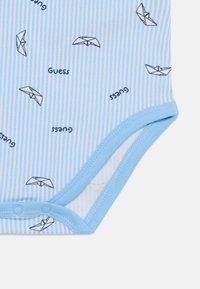 Light blue onesie featuring thin stripes and a repeating pattern of origami boats and the text "Guess" in dark blue. Cotton material with snap closure.