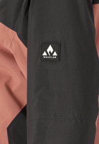 Schwarze und rosa Jacke mit einem dreieckigen Logo-Patch mit der Aufschrift "WHISTLER", matte Oberfläche und kontrastierenden Farbpaneelen.
