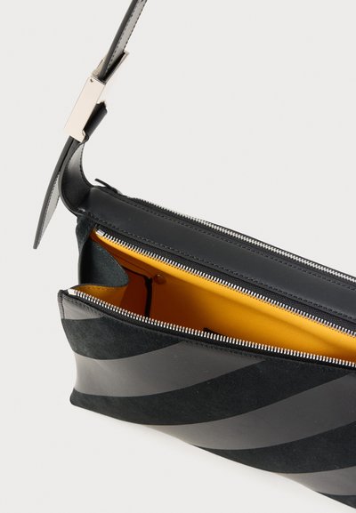 Μαύρη τσάντα crossbody από σουέτ με διαγώνιες ρίγες, ανοιχτό φερμουάρ που αποκαλύπτει φωτεινή κίτρινη εσωτερική επένδυση και ρυθμιζόμενο ιμάντα ώμου με ασημένια αγκράφα.