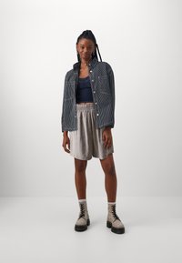Striped denim jacket, dark blue tank top, light gray elastic shorts, and beige combat boots with black laces. Smooth textures and casual fit.