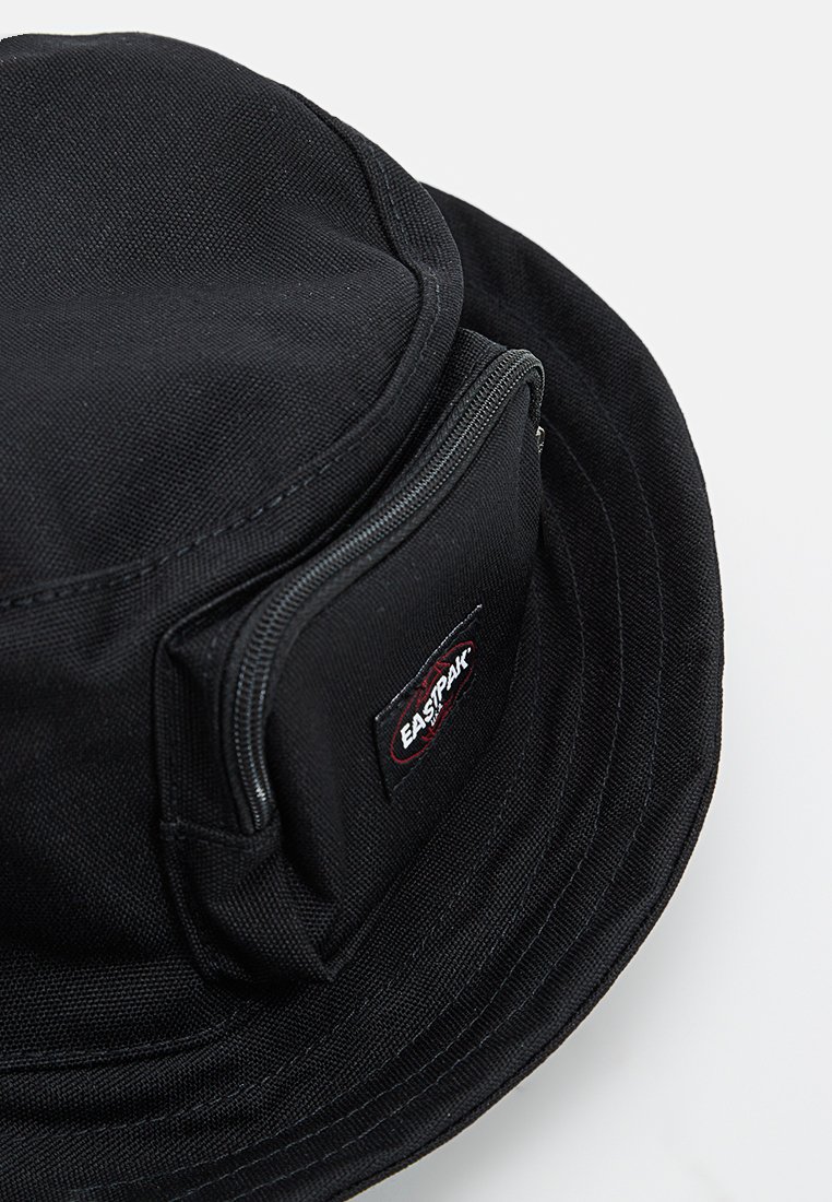 Chapeau seau en tissu noir avec une poche zippée à l'avant arborant un petit patch logo Eastpak.