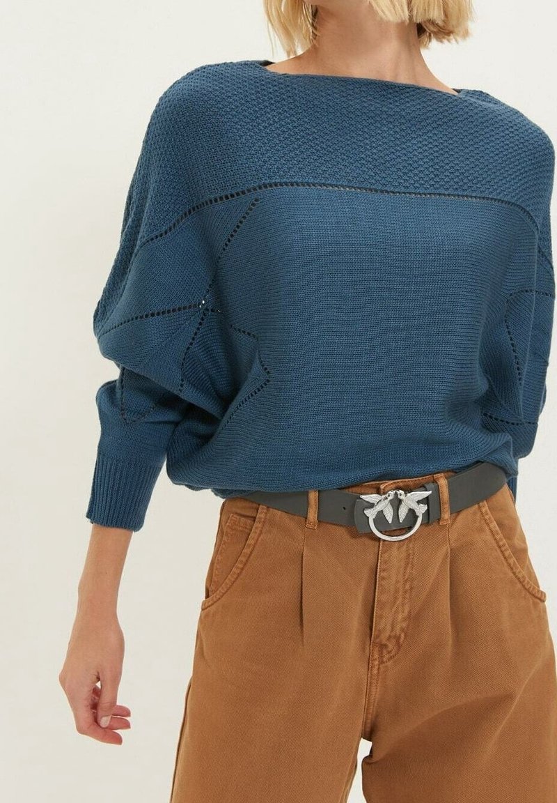 Donkerblauwe gebreide trui met een brede halslijn en een gestructureerd patroon, gecombineerd met bruine high-waisted broek en een decoratieve zilveren riemgesp.