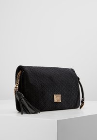 Borsa a tracolla nera trapuntata con un accento a nappina, hardware dorato e una silhouette strutturata. Presenta una tracolla in catena e pelle.