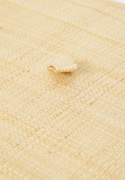 Woven mat od prirodnih vlakana, svijetlosmeđe boje s teksturiranom površinom; sadrži mali dodatak od istog materijala.