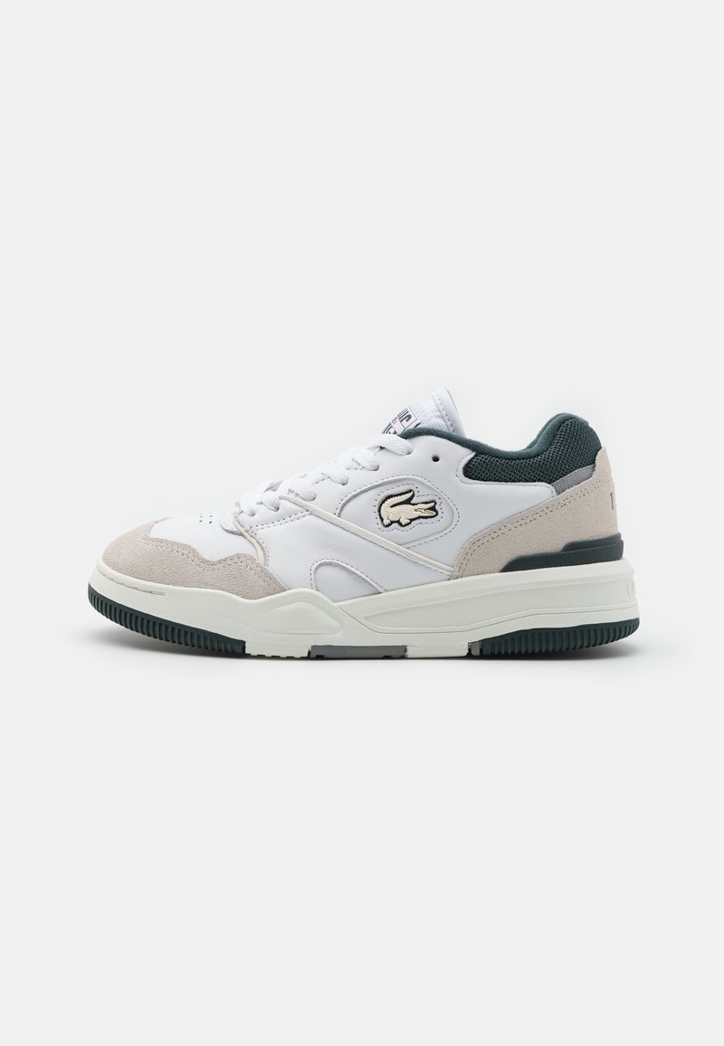 Baskets basses blanches et beiges avec col matelassé vert, semelle texturée, laçage sur le devant et logo crocodile Lacoste sur le panneau latéral.
