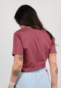 T-shirt marron à manches courtes en coton, avec un col rond et une petite étiquette de marque sur l'épaule gauche.