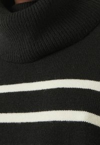 Black turtleneck sweater with ribbed texture, featuring two horizontal white stripes across the chest. Soft knit fabric, rounded collar.
