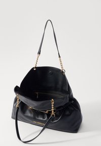 Black leather handbag with a slouchy design, gold chain accents, and a zippered interior pocket. Features a single shoulder strap.