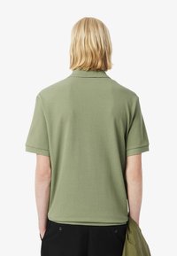 Polo shirt verde oliva a maniche corte con una consistenza morbida, colletto e polsini piegati. Presenta un design semplice, adatto per un look casual.