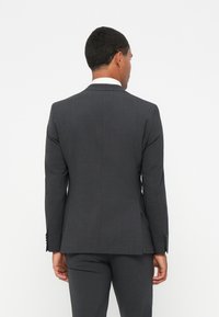 Giacca da abito grigio scuro con vestibilità sagomata, revers a punta, spacco singolo e polsini abbottonati, abbinata a pantaloni coordinati.