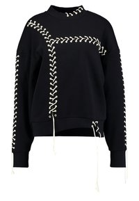 Musta huppari, jossa on korkea kaulus, jossa on kermaista nauhakiinnitystä sivuilla ja helmassa, sekä säädettävät nauhat alaosassa.