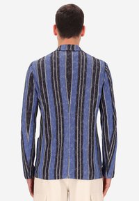 Giacca a righe blu e nere con tessuto strutturato, caratterizzata da motivi verticali e con colletto a scollo a V. Dettagli di cucitura pronunciati lungo le cuciture.