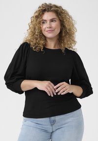 Czarna, teksturowana bluzka z poduszkowanymi rękawami, okrągłym dekoltem i dopasowanym dołem. Połączona z jasnoniebieskimi dżinsami. Brak widocznych wzorów lub akcentów.