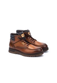 Bottines en cuir marron avec accents noirs, semelle en caoutchouc, design à lacets et col rembourré. Présente des coutures renforcées et un détail de logo.