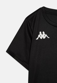 T-shirt noir à manches courtes en tissu lisse. Présente un logo blanc de deux silhouettes dans le coin supérieur gauche. Conception à coupe régulière.