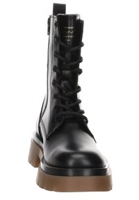 Stivale in pelle nera con lacci, caratterizzato da una zip frontale, suola piatta robusta marrone e dettagli di cucitura tono su tono. Texture liscia e design elegante.