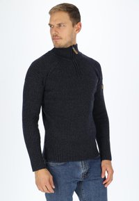Ribbed navy knit sweater with a high collar and zip closure. Features long sleeves and a fitted shape. Textured fabric gives a warm appearance.