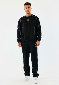 Conjunto de sudadera y pantalones negros con acentos de costura en azul claro. Presenta un cuello redondo y puños elásticos. Combinado con zapatillas blancas.