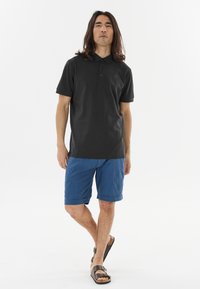 Sort polo shirt med tre-knap lukning, blå shorts med opsmøget kant og brune sandaler. Glat stof med en afslappet pasform.