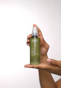 Nettoyant crème purifiant Aveda Botanica Kinetics dans une haute bouteille en verre vert transparent avec un bouchon-pompe blanc. Capacité : 5 oz fluide.