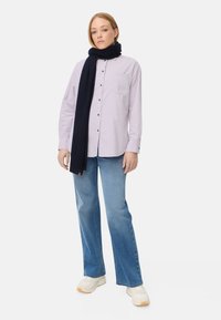 Helles lila Hemd mit Brusttasche, kombiniert mit hellblauen Schlagjeans und einem dunkelblauen Schal, abgerundet mit weißen Sneakers.