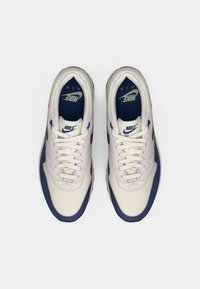 Valge ja tumesinine Nike Air spordijalatsite paar, vaadatuna ülevalt, lükatud esiosad ja bränditud sissekatted, valgel taustal.