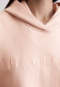 Felpa rosa chiaro realizzata in tessuto morbido, dotata di cappuccio e con logo ricamato "Marc O'" sul davanti. Texture liscia con cuciture sottili.