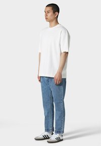 Hvit t-skjorte med korte ermer, avslappet passform. Lys blå denim jeans med rett snitt. Svart og hvite joggesko med tre striper.