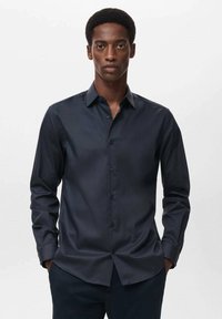 Temno modra srajca s kratkimi in dolgimi rokavi ter klasičnim ovratnikom. Ponaša se s slim fit krojem in usklajenimi gumbi.
