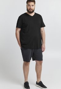 Fekete v-nyakú póló rövid ujjakkal, puha anyagból készült. Szürke rövidnadrággal és fekete sportcipővel párosítva; laza öltözet.