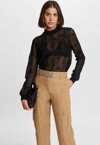 Zwarte kanten top met lange mouwen en een rimpelende halslijn, laag over een nauwsluitend zwart ondergoed; gecombineerd met beige high-waisted cargobroeken.