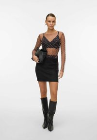 Sheer black long-sleeve top with bead detailing, paired with a black mini skirt and knee-high black boots. Holding a black clutch.