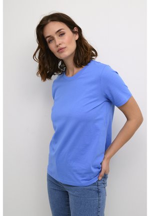 T-shirt en coton bleu avec un col rond et des manches courtes, affichant une coupe standard et une texture lisse. Porté avec un jean en denim clair.