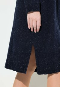 Námořnická modrá pletená šaty s texturovaným materiálem a žebrovanými manžetami. Obsahuje postranní rozparek pro usnadnění pohybu. Materiál vykazuje jemné tečky.