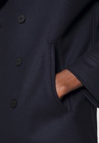 Abrigo de mezcla de lana en color navy con diseño de doble breasted, botones negros y bolsillos laterales. Textura suave y mangas ajustadas.