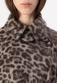 Ullkåpe med leopardmønster som har høy krage, fremtredende knappdetaljer, og et mykt, teksturert stoff i nyanser av brunt og beige.