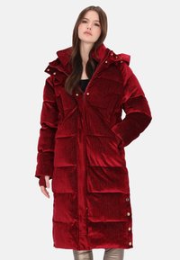 Piros kordbársony steppelt kabát magas gallérral, patentgombos részletekkel és nagy elülső zsebekkel. Puha tapintású, fényes felületű.