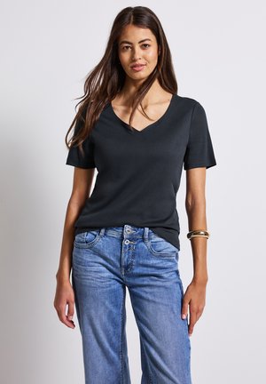 T-shirt nera a V con maniche corte, realizzata in tessuto liscio. Abbinata a jeans a gamba larga blu chiaro e un bracciale d'oro al polso.