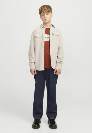 Light gray button-up shirt with two chest pockets, red graphic t-shirt underneath, dark blue denim pants, and black lace-up shoes.