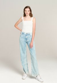 White square-neck tank top paired with light blue high-waisted jeans and white sneakers. The jeans have a faded finish and wide legs.