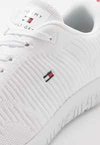 Valkoiset lenkkarit, joissa on teksturoitu verkkopinta, pienellä värillisellä logopatchillä sivulla ja kiinteä valkoinen pohja, jossa on kuvioitu pintakuvio.