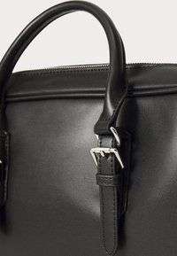 Black leather handbag with a smooth texture, a zipper closure, and a buckle detail on the strap, featuring rounded double handles.